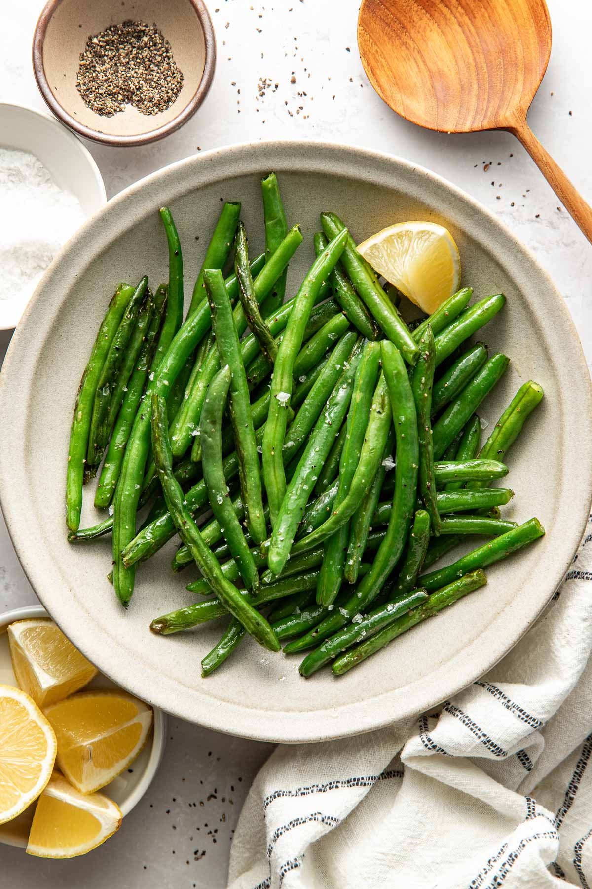 Overhead view of a dish filled with fresh Sautéed Green Beans sprinkled with flakey sea salt and garnished with a lemon wedge.