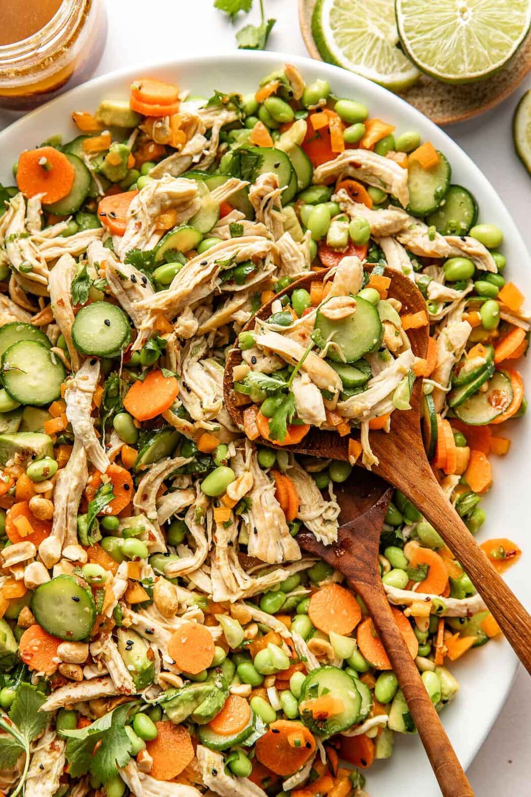 Close up view of a bowl of Thai Chicken Salad With Edamame and two wooden spoons stuck into the side.