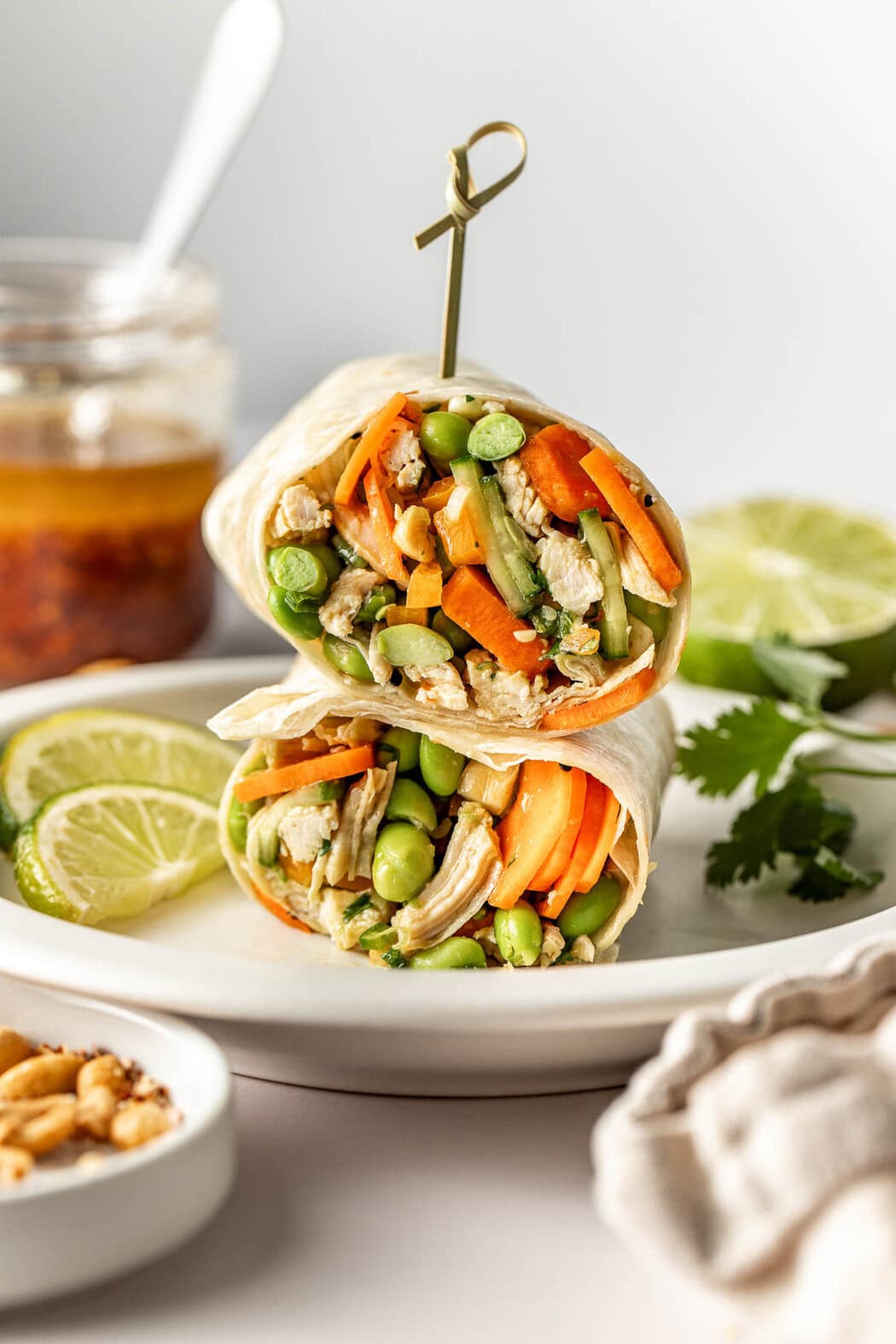 Close up view of a plate with a Thai Chicken Salad wrap stacked and a toothpick going through the top.
