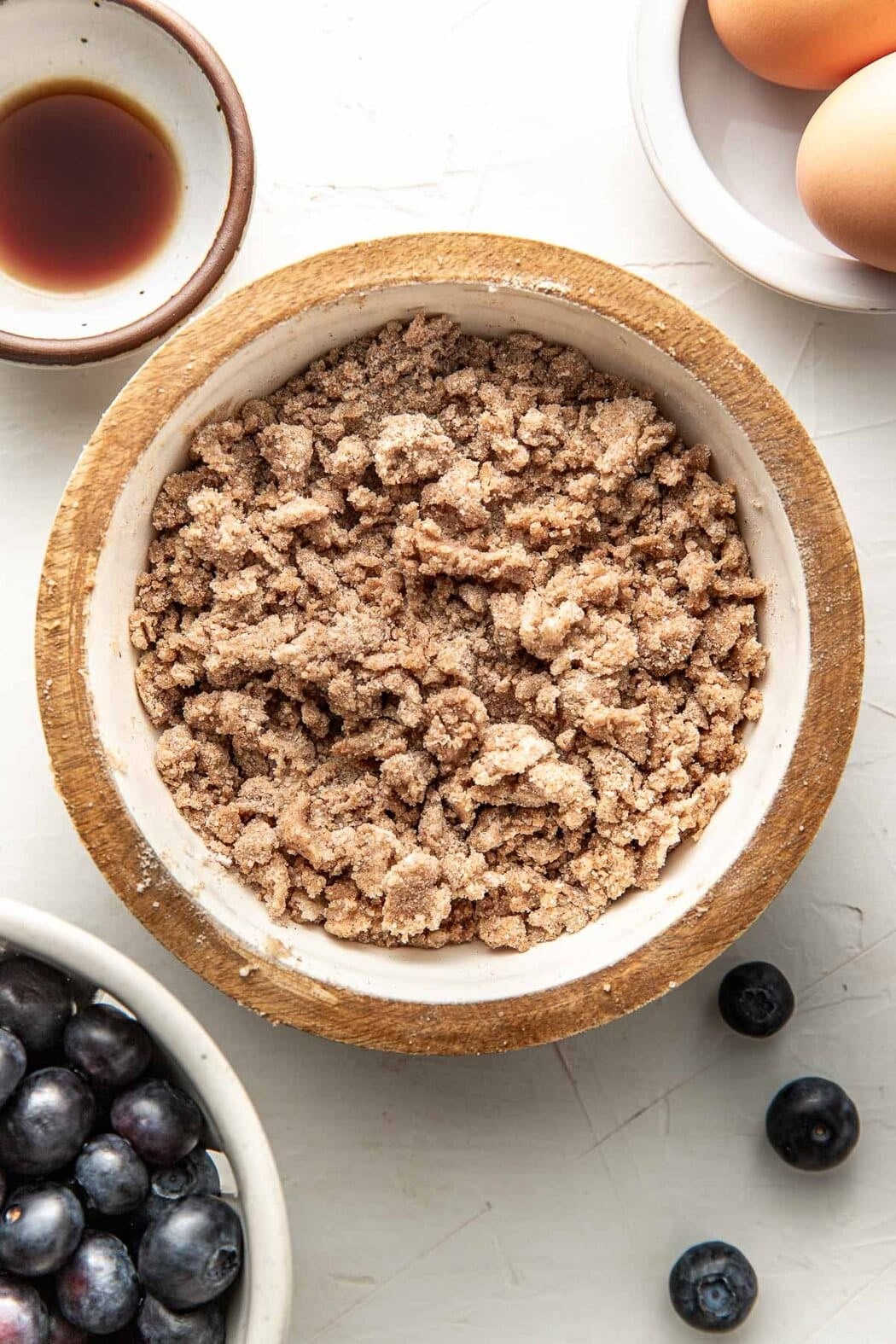 Overhead view of a bowl of crumble topping next to a small bowl of fresh blueberries.