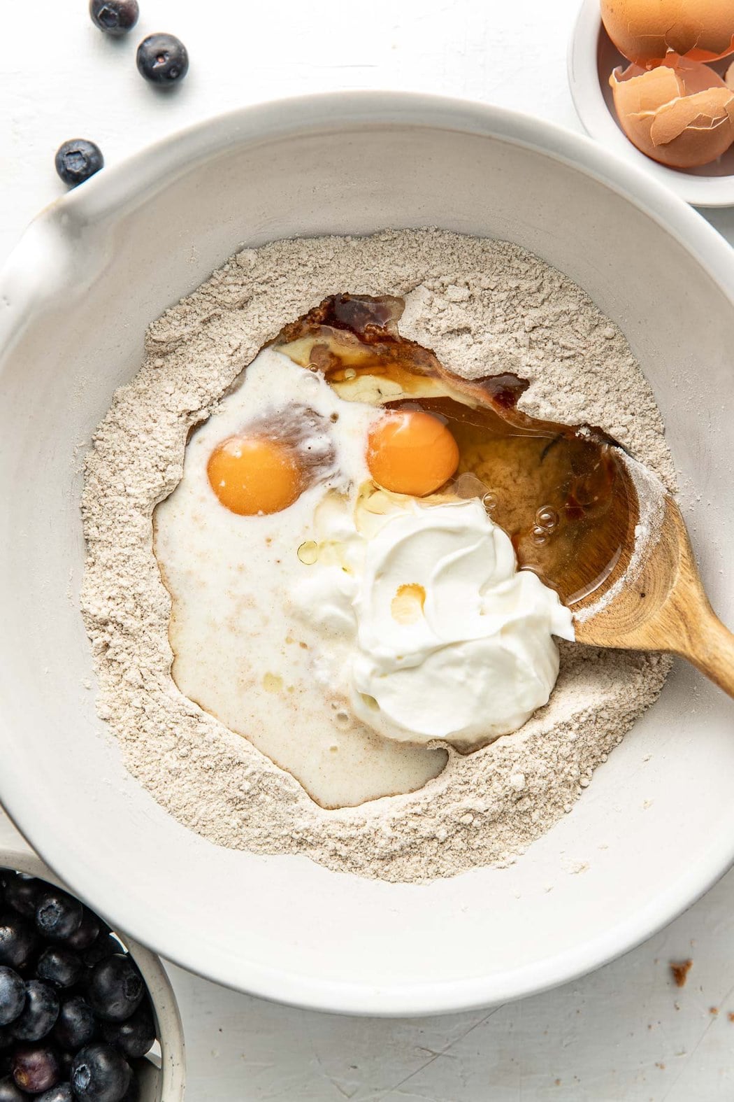 Overhead view of a bowl of flour and eggs ready for mixing with a wooden spoon in the side.