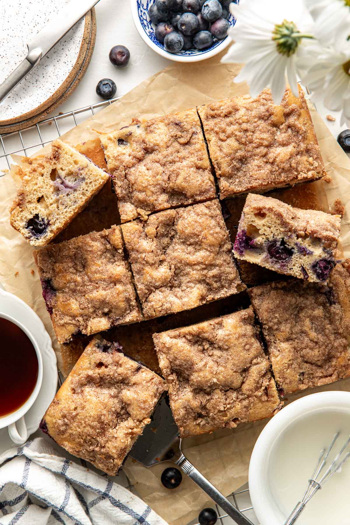 Overhead view of a freshly baked Blueberry Coffee Cake cut into squares and sitting on parchment paper on top of a wire cooling rack.