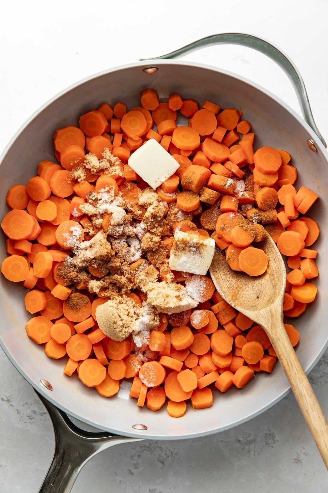 Overhead view of a skillet filled with sliced carrots topped with some brown sugar and butter.