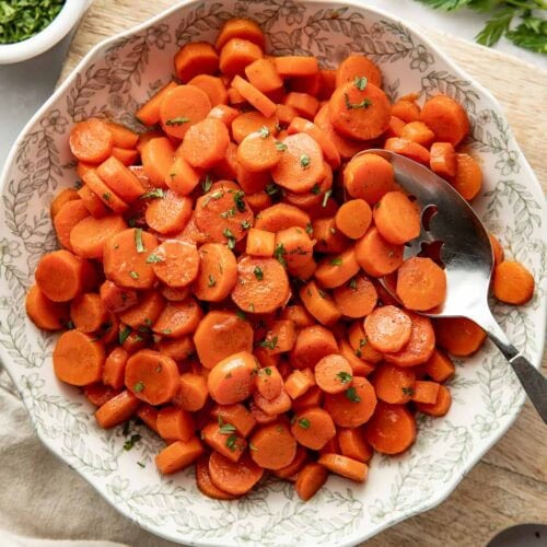Overhead view of a bowl filled with sliced cooked carrots topped with fresh herbs and a coating of sweet glaze.