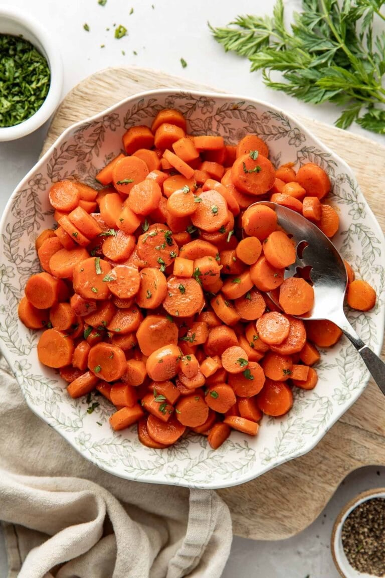 Overhead view of a bowl filled with sliced cooked carrots topped with fresh herbs and a coating of sweet glaze.