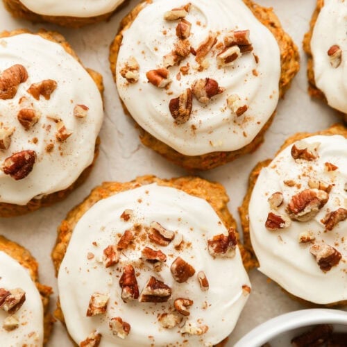 Overhead view of carrot cake cookies topped with a cream cheese frosting and sprinkled with walnuts and cinnamon.