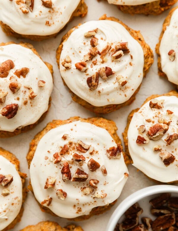 Overhead view of carrot cake cookies topped with a cream cheese frosting and sprinkled with walnuts and cinnamon.