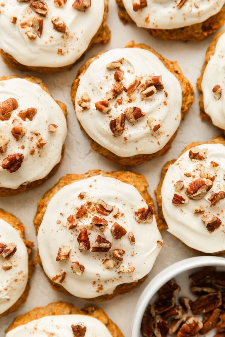 Overhead view of carrot cake cookies topped with a cream cheese frosting and sprinkled with walnuts and cinnamon.