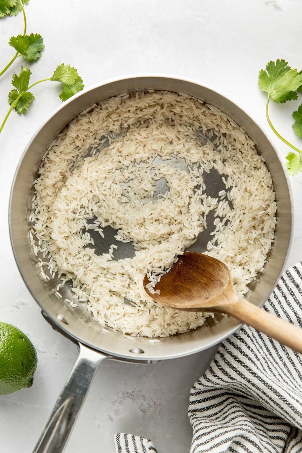 Overhead view of a pot of rice being stirred with a wooden spoon.