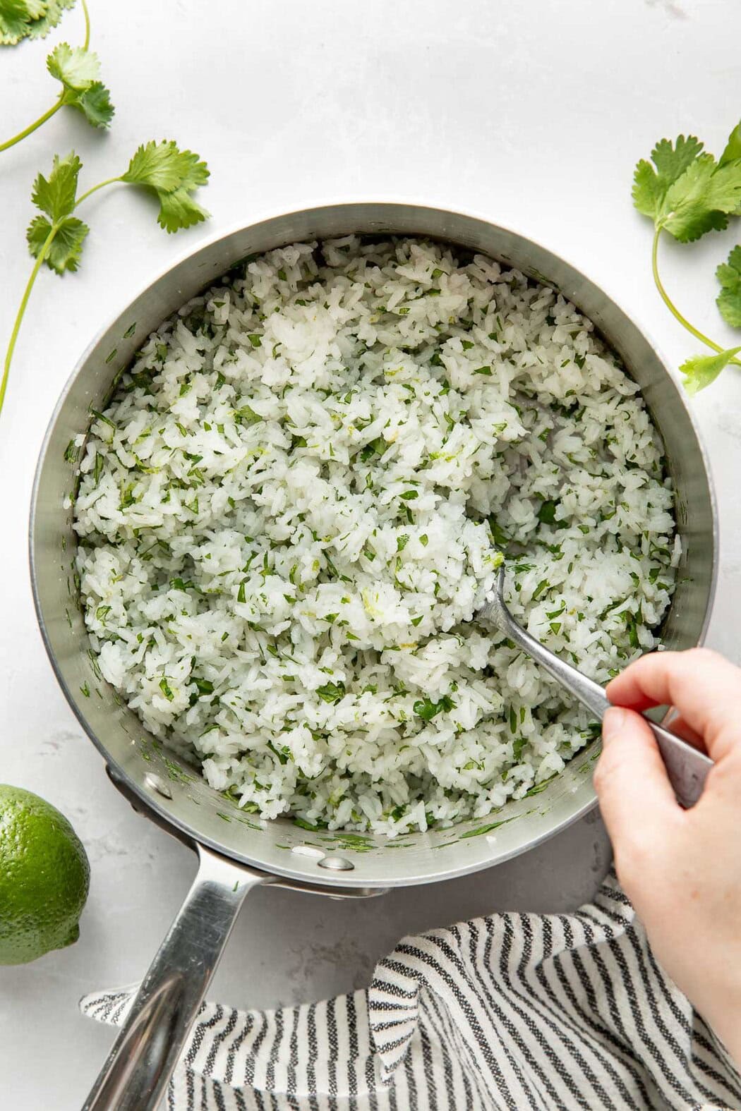 Overhead view of a pot filled with freshly cooked Cilantro Lime Rice being stirred with a metal spoon.