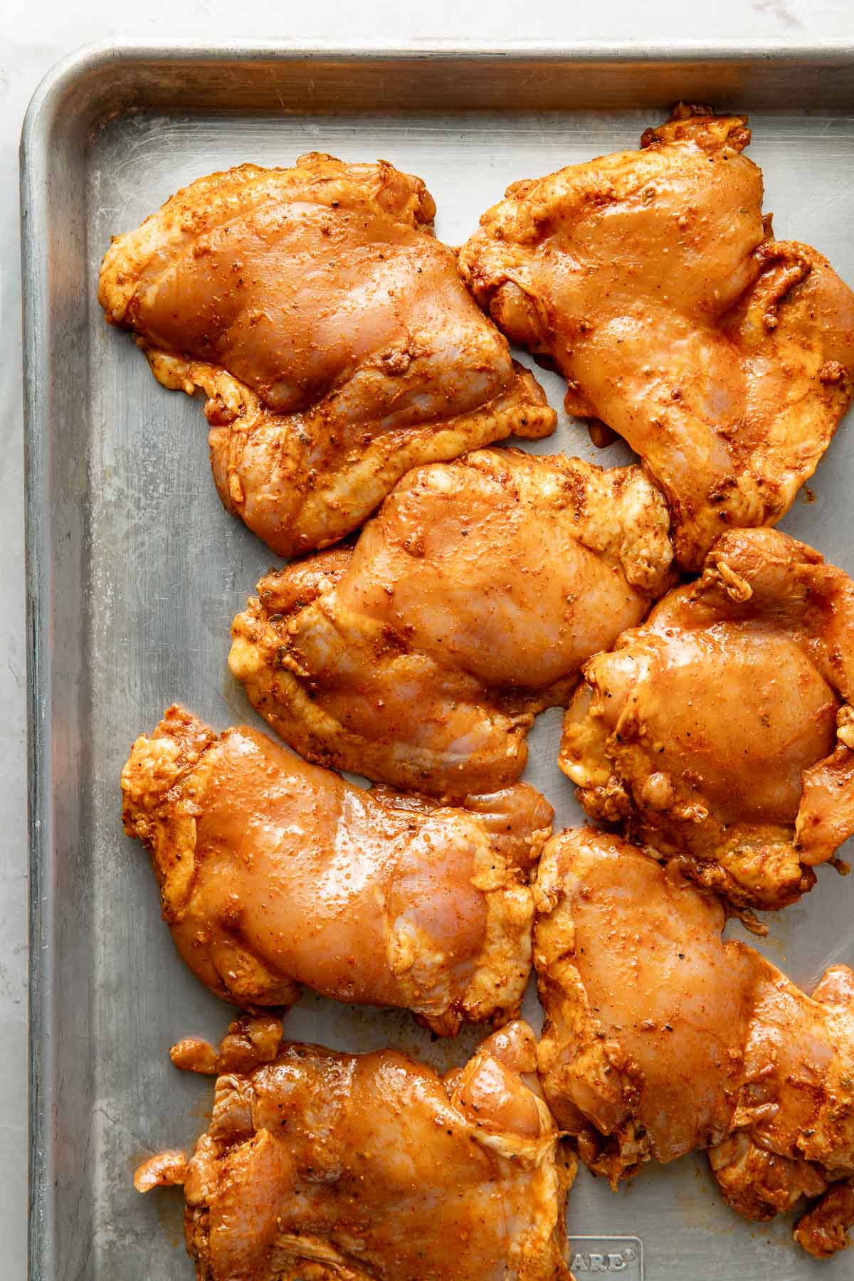 Overhead view of a sheet pan of seasoned chicken thighs ready for cooking.