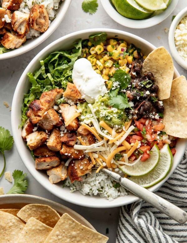 Overhead view bowl filled with chipotle chicken, rice, corn salsa, black beans, cheese, sour cream, and guacamole