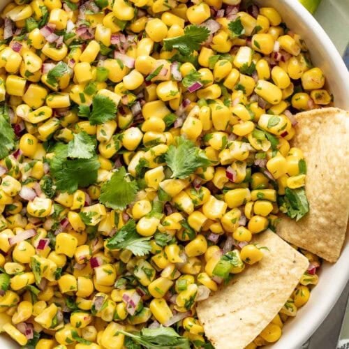 Overhead view of a bowl of corn salsa topped with fresh cilantro and garnished with lime.