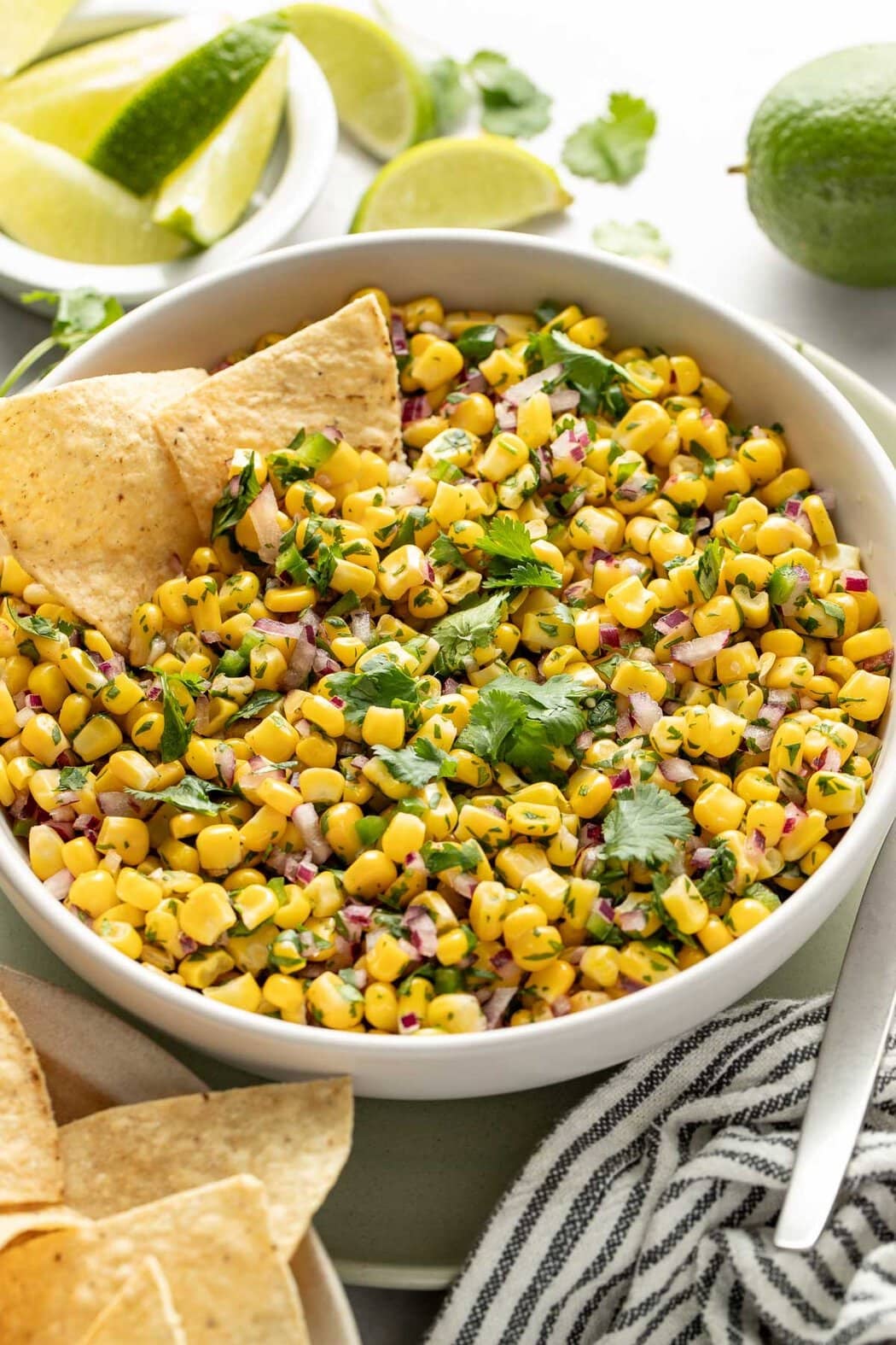 Close up view of a bowl of Copycat Chipotle Corn Salsa topped with fresh cilantro and garnished with limes and corn tortilla chips.