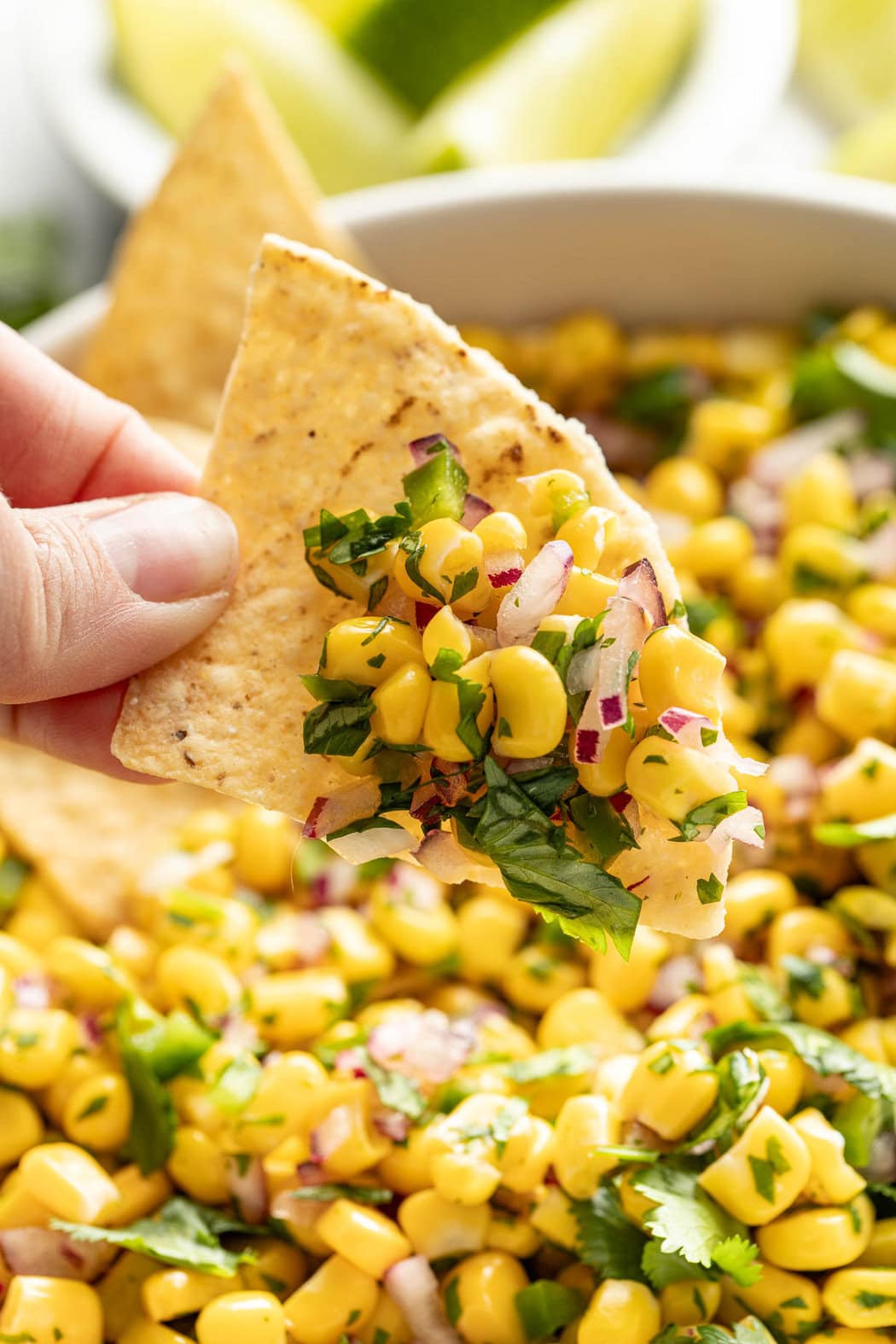 Close up view of a hand holding a tortilla chip filled with Copycat Chipotle Corn Salsa.