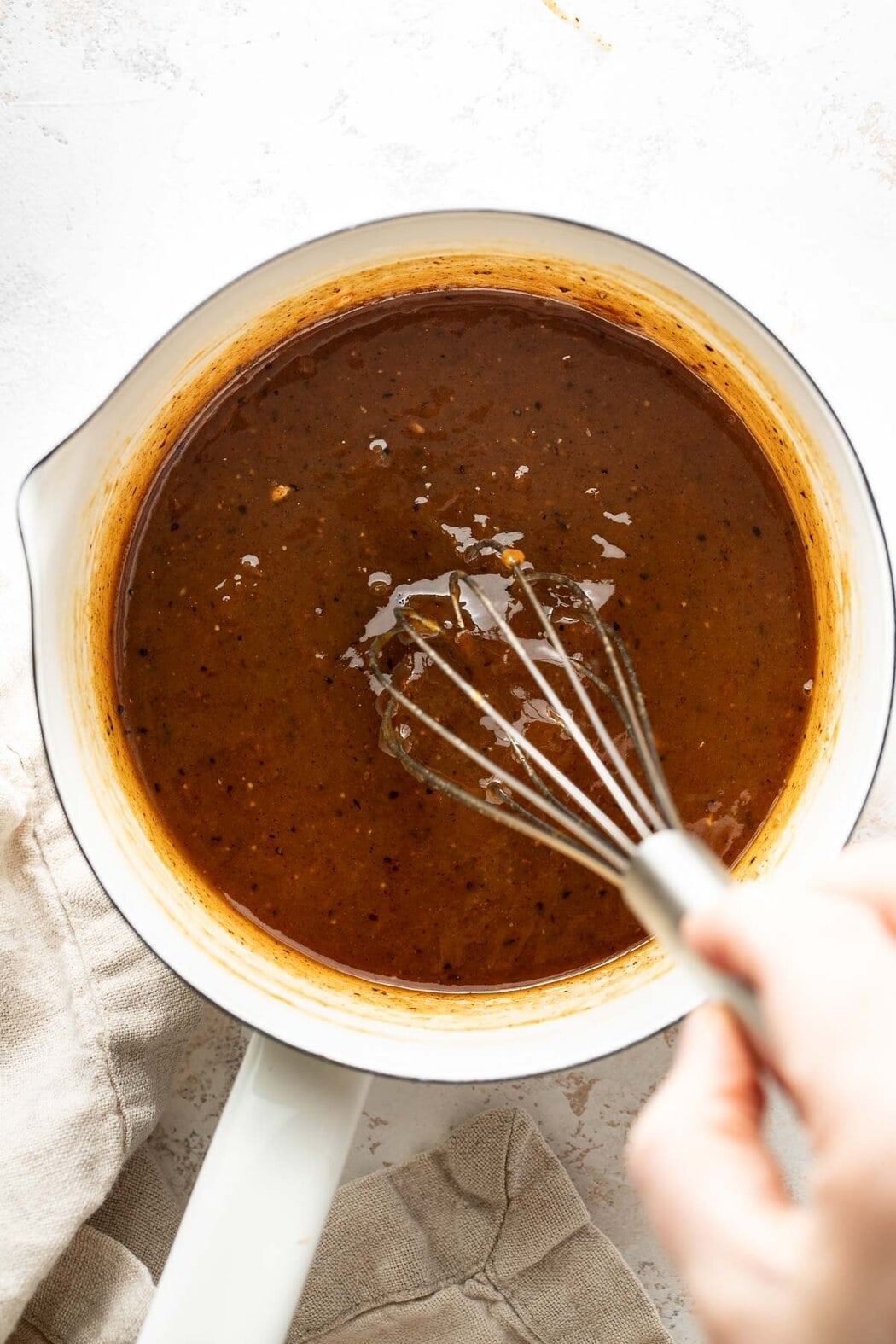 Overhead view of a saucepan filled with a ham glaze being whisked with a metal whisk.