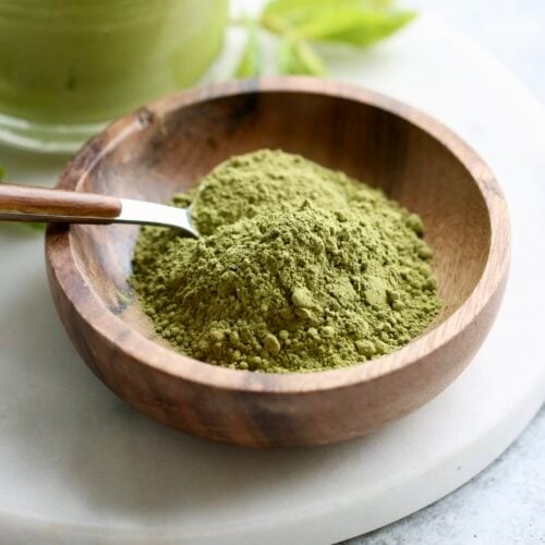 Close up view of a small dish of green matcha powder with a spoon in the dish.