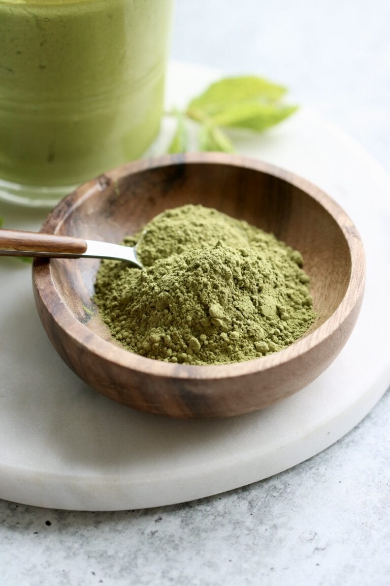 Close up view of a small dish of green matcha powder with a spoon in the dish.