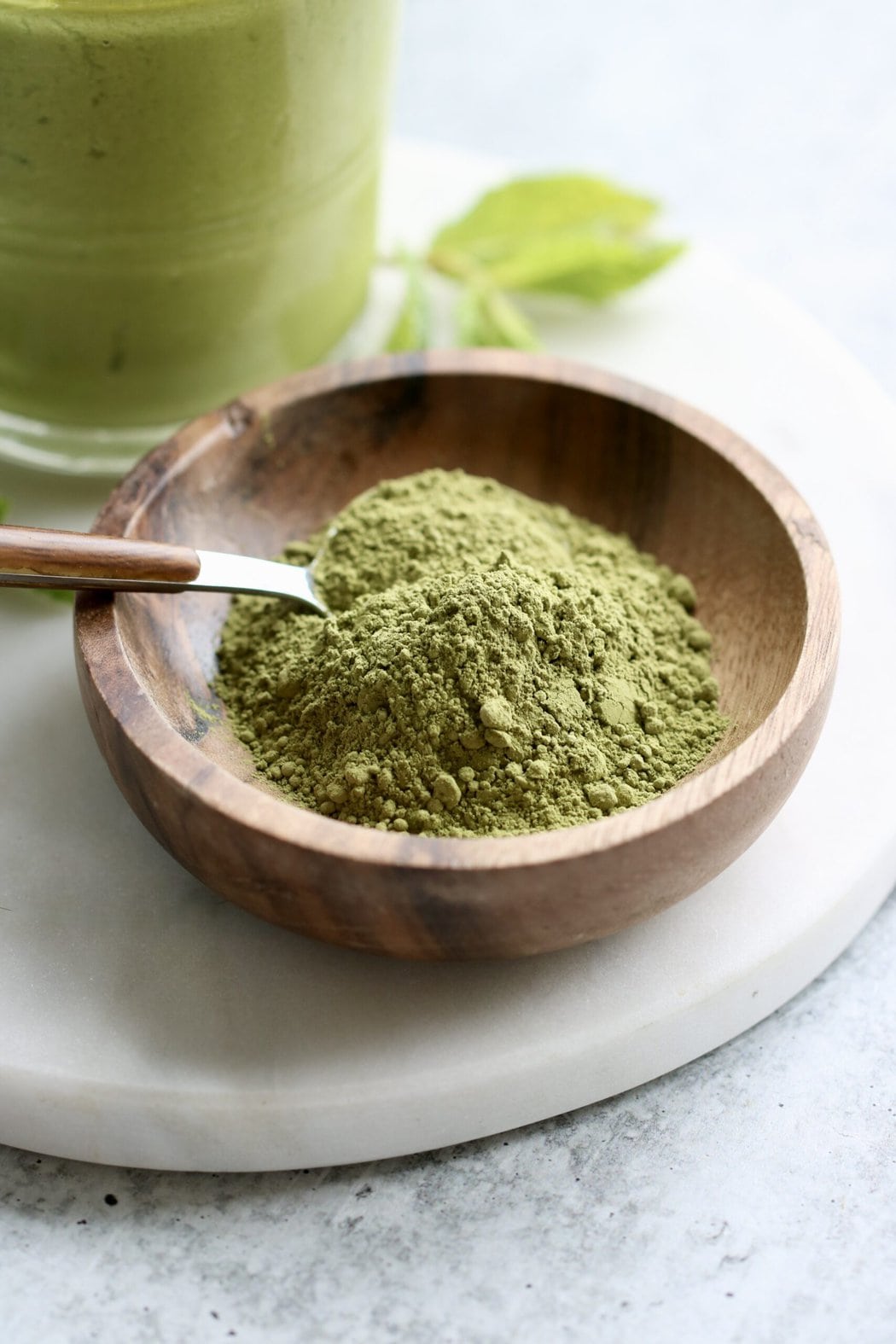 Close up view of a small wooden dish filled with green matcha powder with a spoon stuck into the powder.