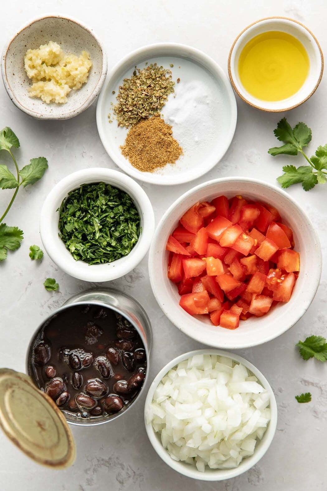 Overhead view of a variety of ingredients for Mexican Black Beans in different sized bowls.