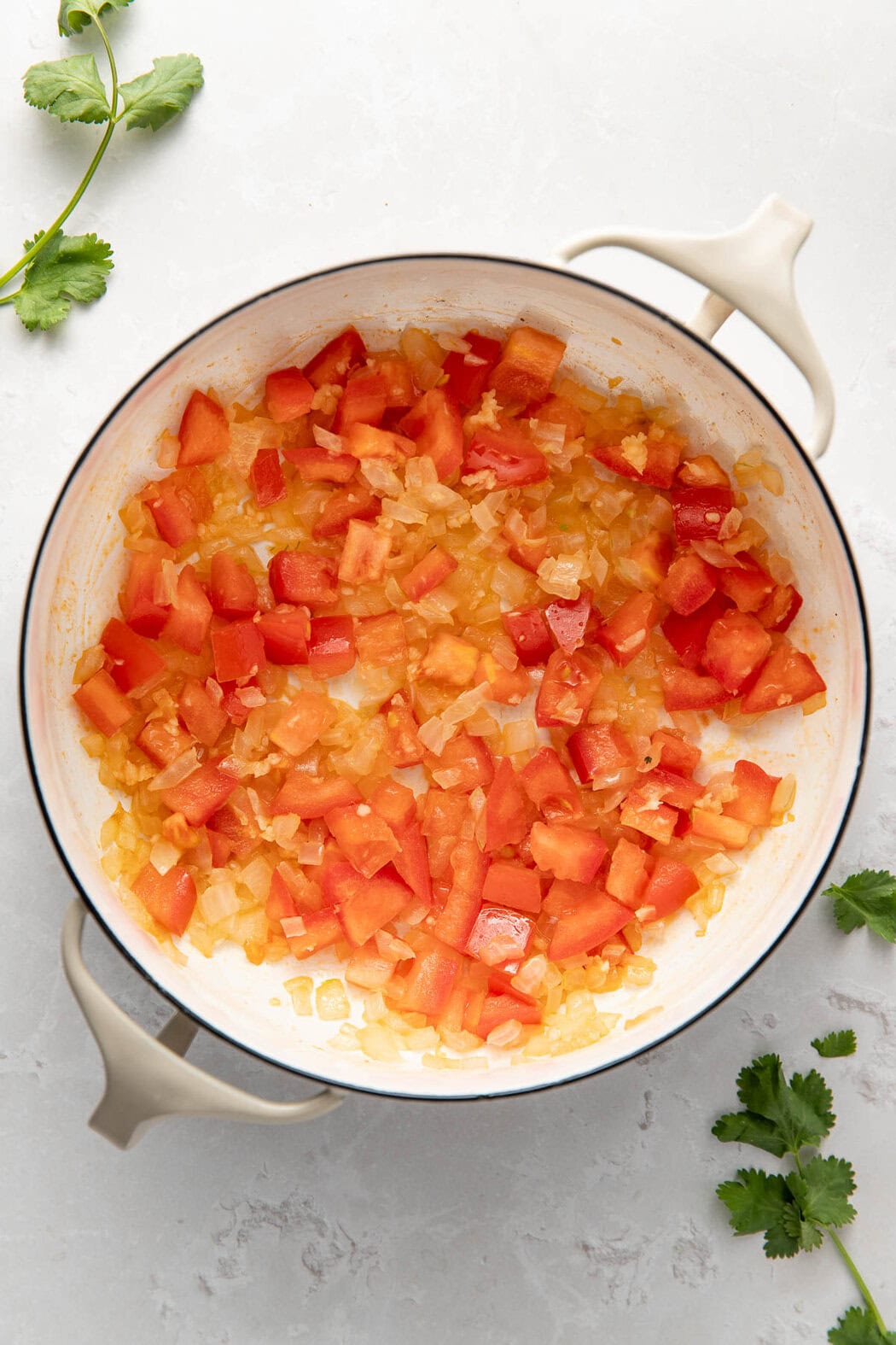 Overhead view of a skillet filled with diced onions and Roma tomatoes sautéing.