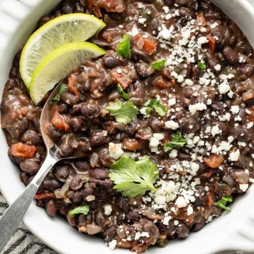 Overhead view of a bowl of Mexican Black Beans topped with cheese crumbles and garnished with lime wedges.