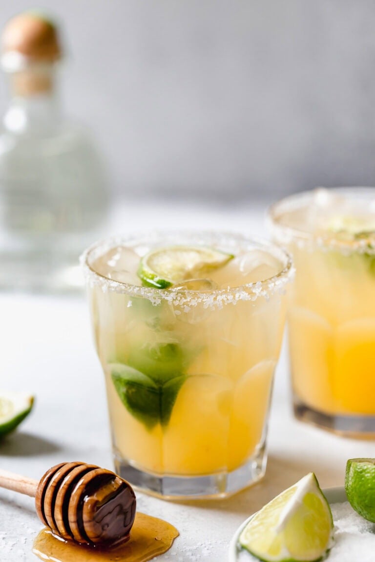 Close up view of two margaritas in salted rimmed glasses topped with lime wedges. 