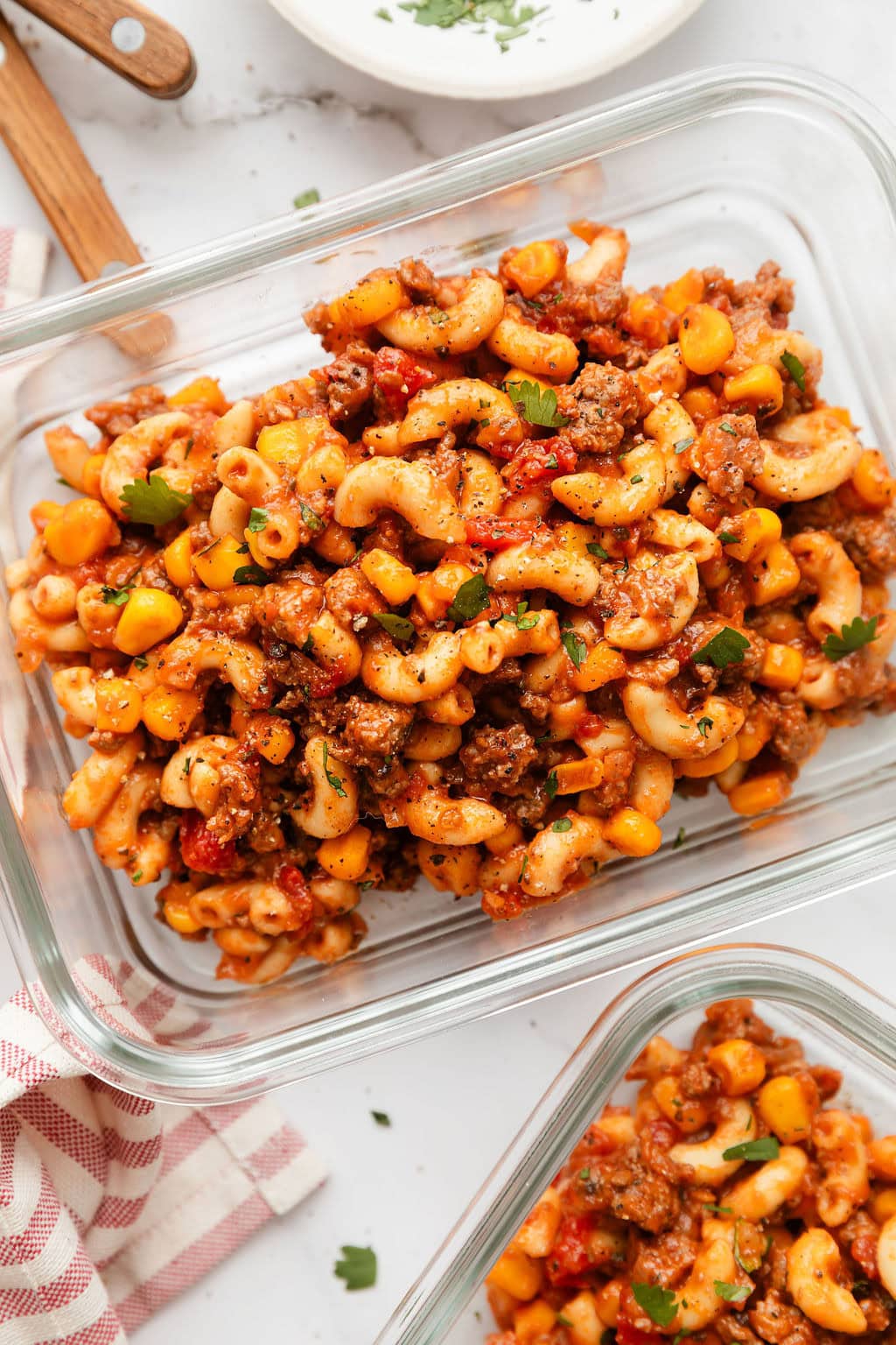 Overhead view of two glass meal prep containers filled with goulash and sprinkled with black pepper and parsley.