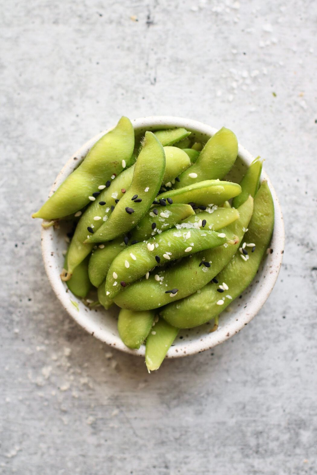 Overhead view of a dish of edamame sprinkled with sesame seeds.