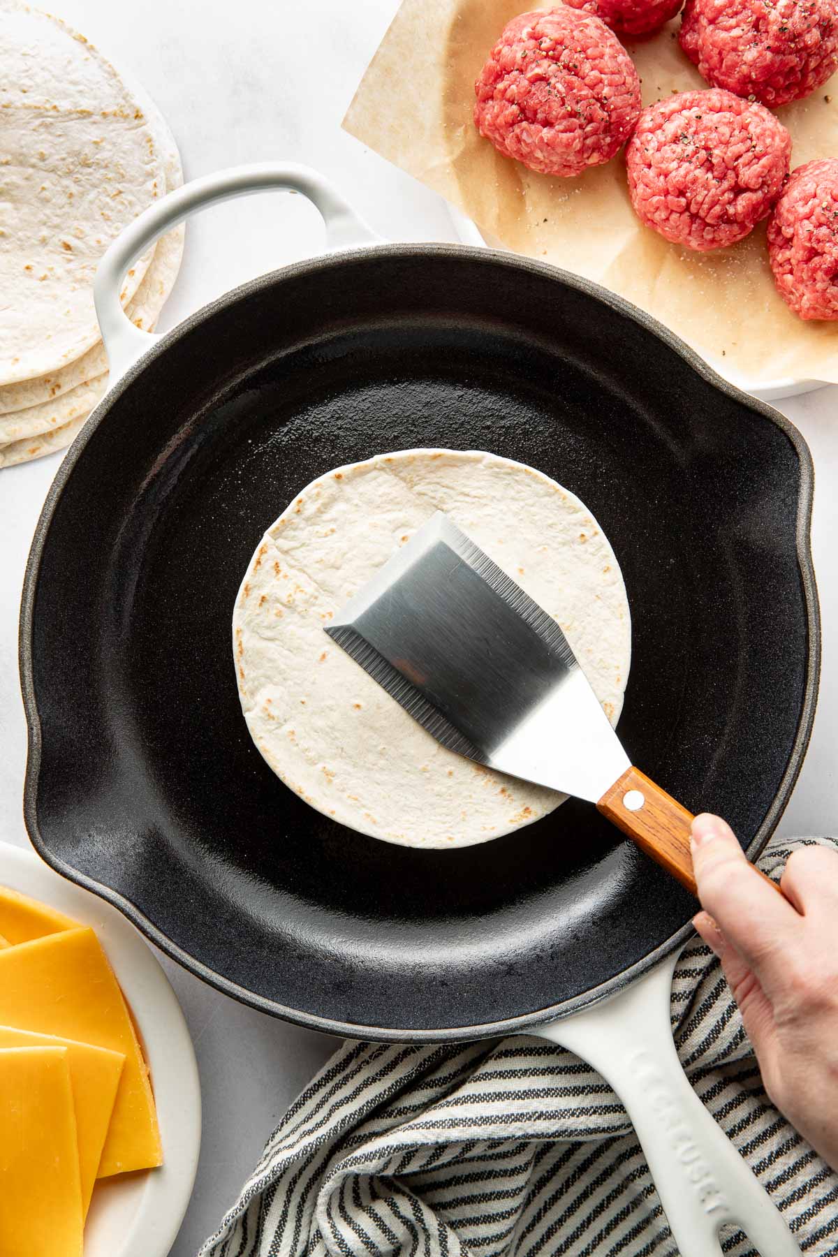Overhead view of a fry pan with a tortilla in it and a spatula pressing it down.