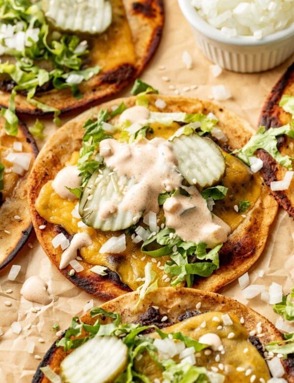 Side view of a smash burger taco lying on parchment paper topped with pickles and sauce