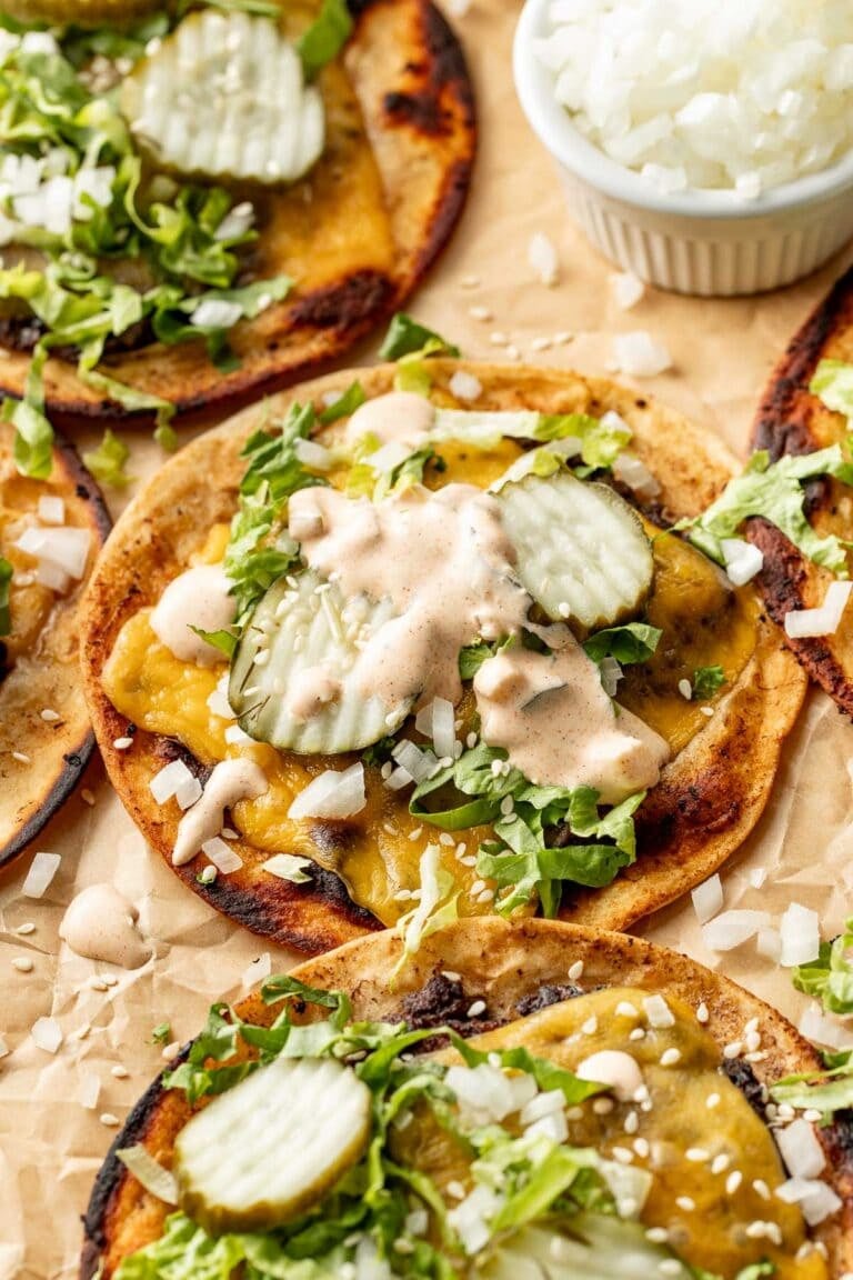 Side view of a smash burger taco lying on parchment paper topped with pickles and sauce
