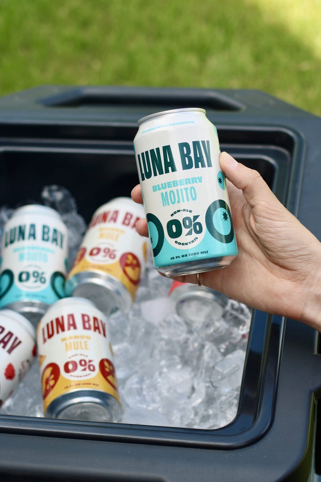Overhead view of a hand holding a canned luna bay mojito over a cooler filled with ice.