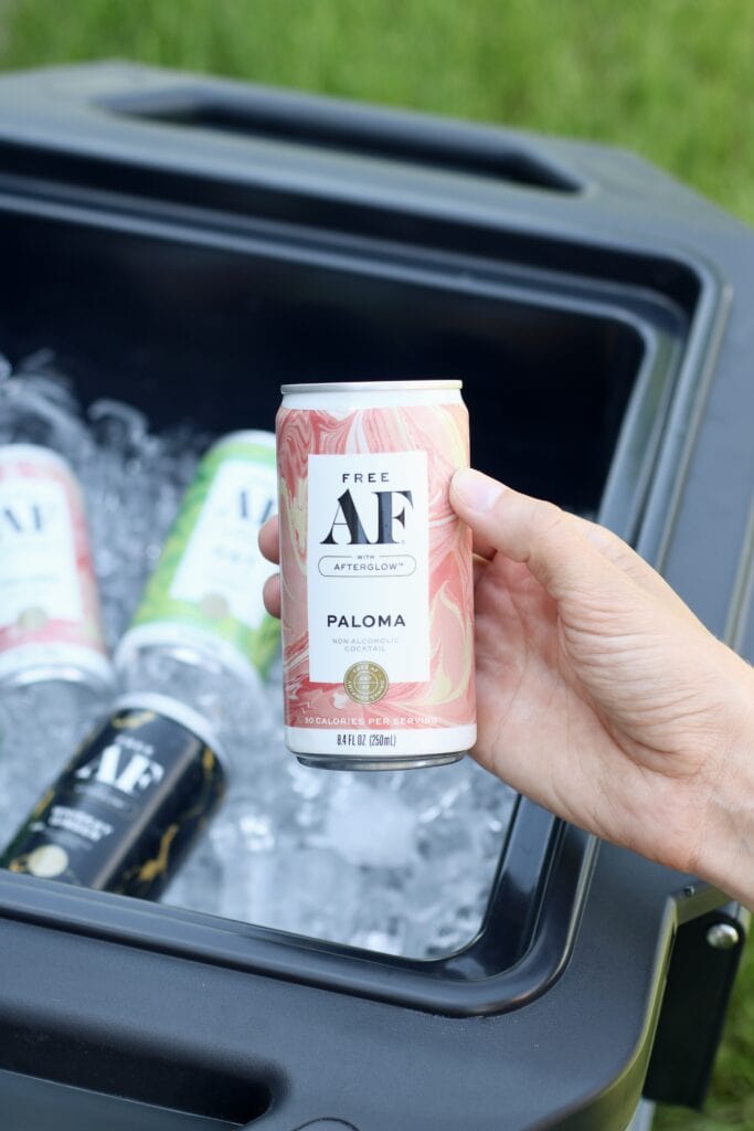 Close up view of a hand holding a canned paloma over a cooler of ice.