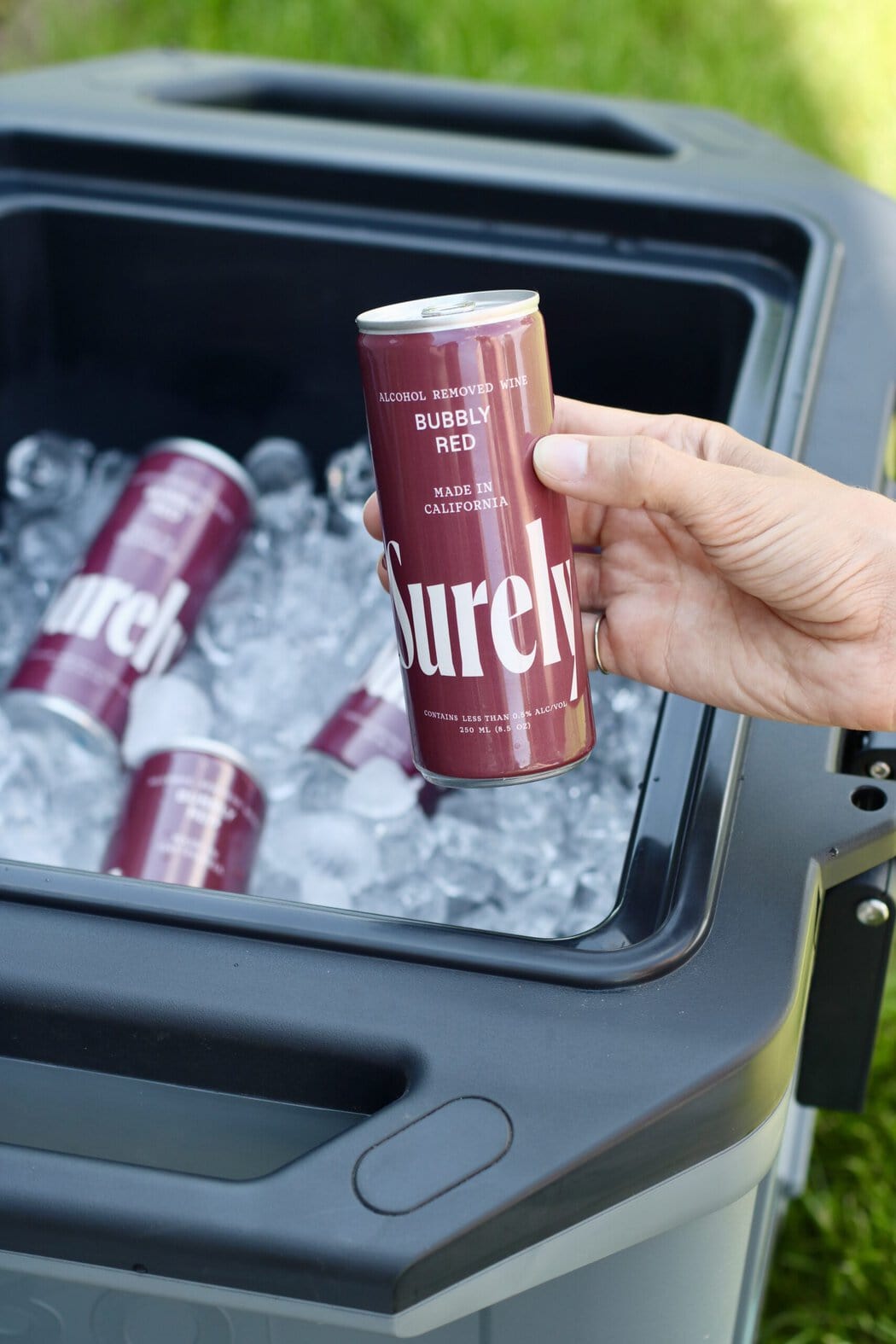 Overhead view of a cooler filled with ice and a hand holding a bubbly red surely can.