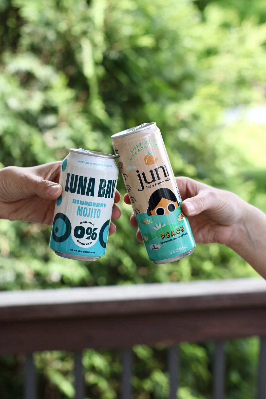 Two hands holding canned mocktails cheering each other.