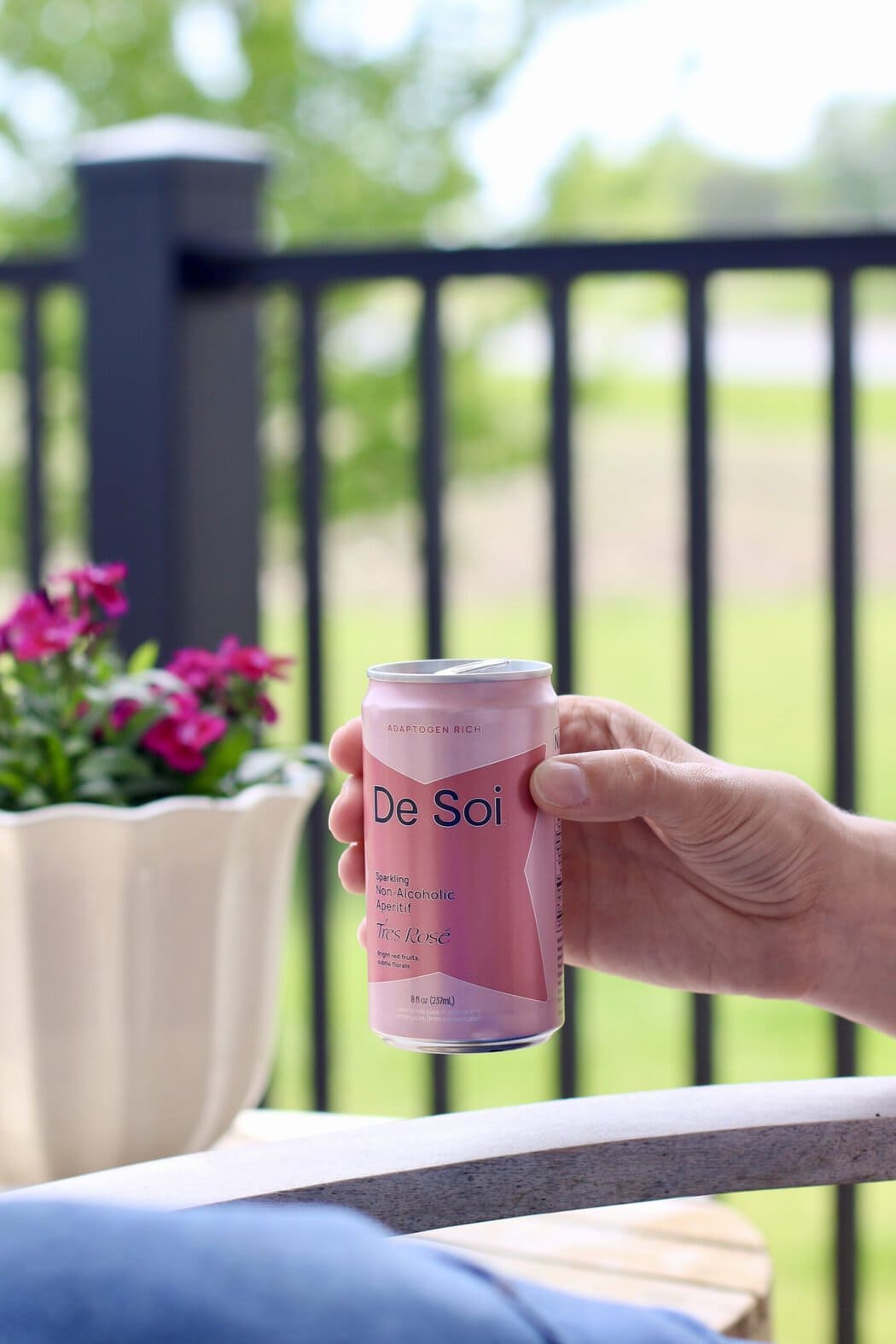 Close up view of a hand holding a pink canned De Soi mocktails with a flower in the background.