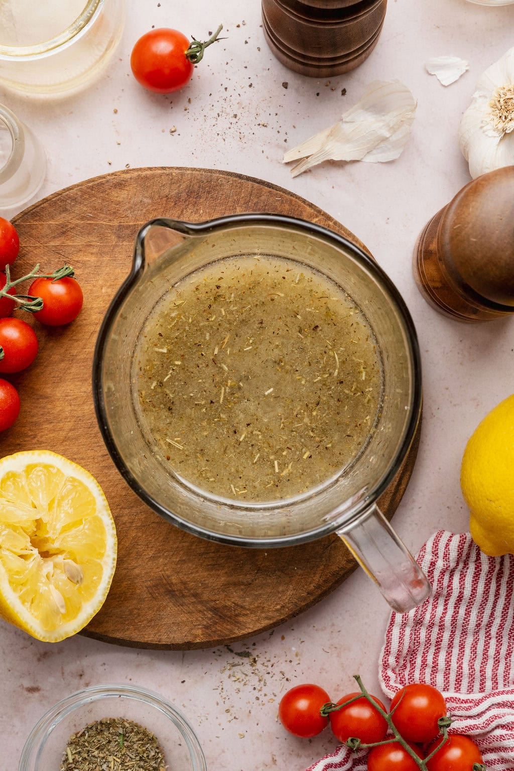 Overhead view of a measuring glass filled with Italian Dressing next to cut lemons and grape tomatoes on a cutting board.