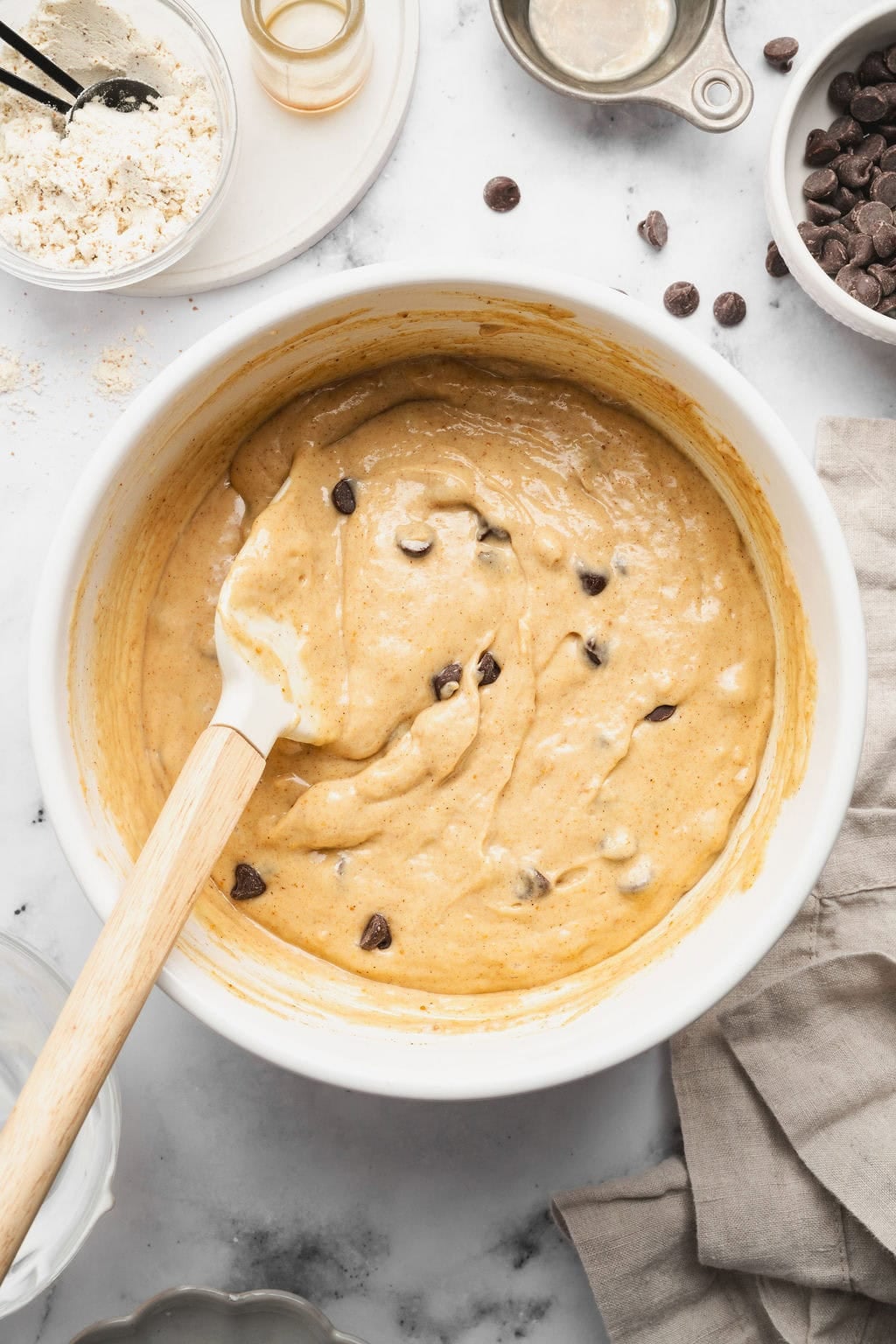 Overhead view of a white bowl of Peanut Butter Protein Muffin batter with a spatula stirring the mixture.