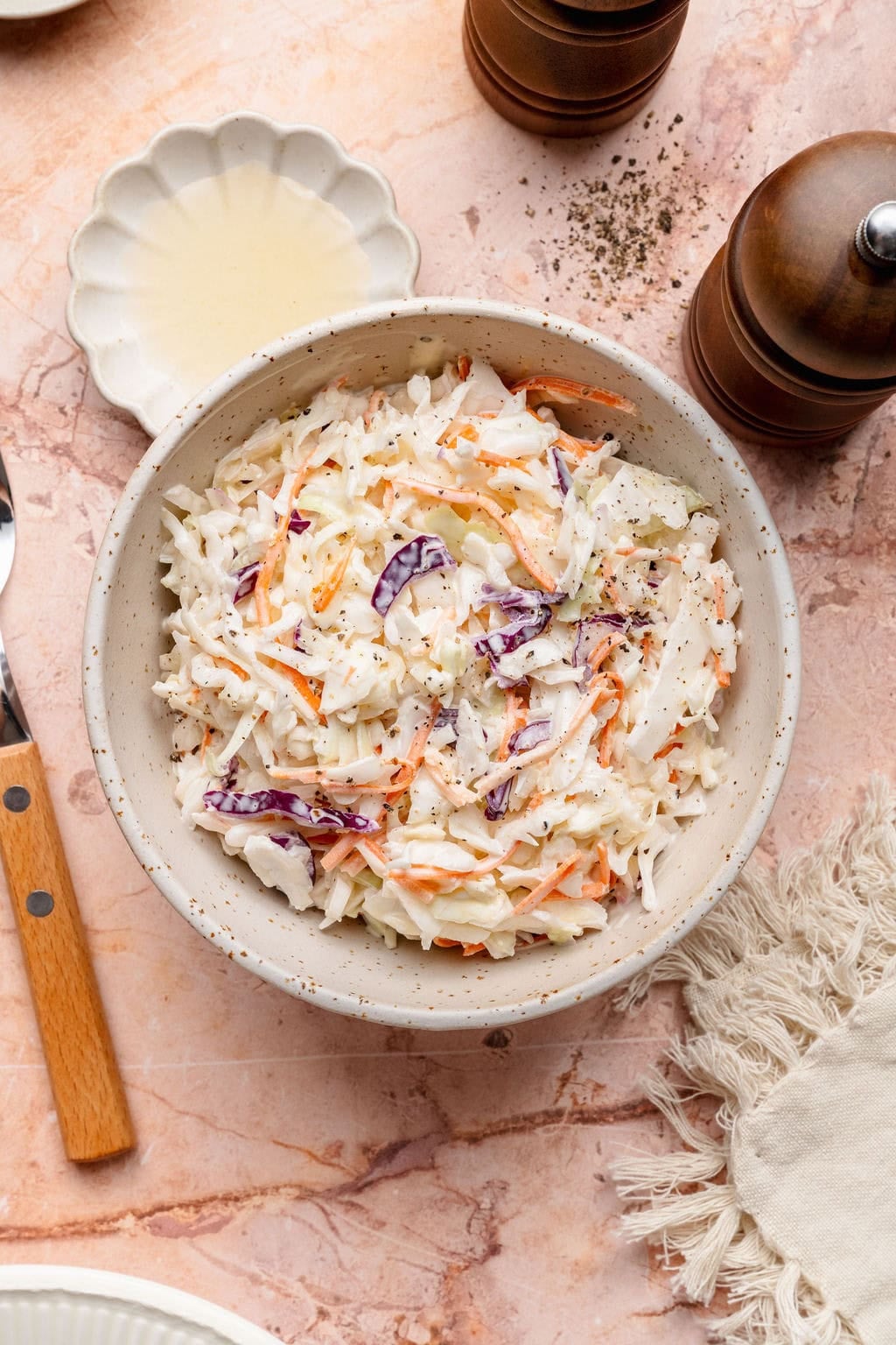 Overhead view of a white bowl of creamy coleslaw topped with black pepper.