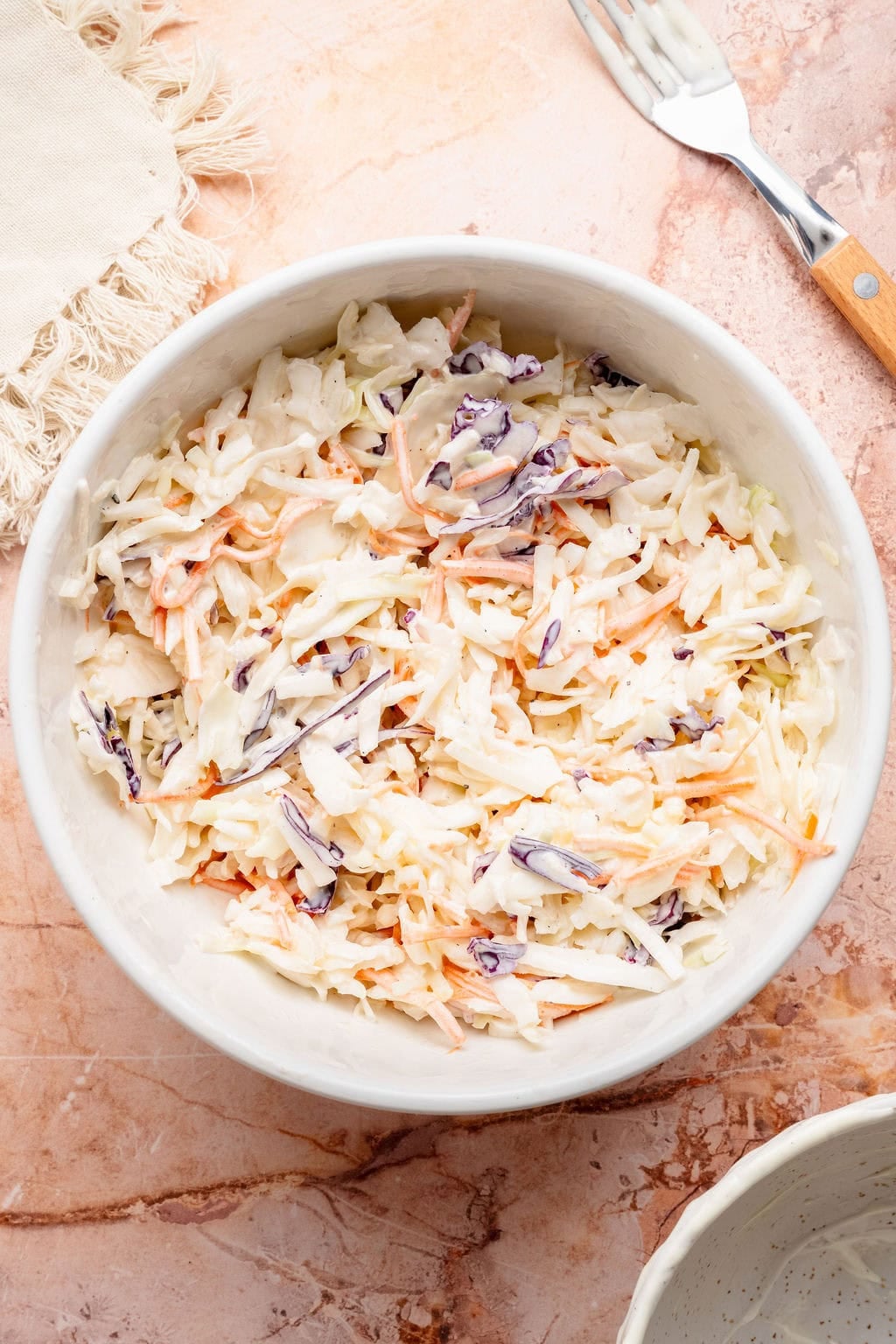 Overhead view of a white bowl filled with fresh coleslaw.