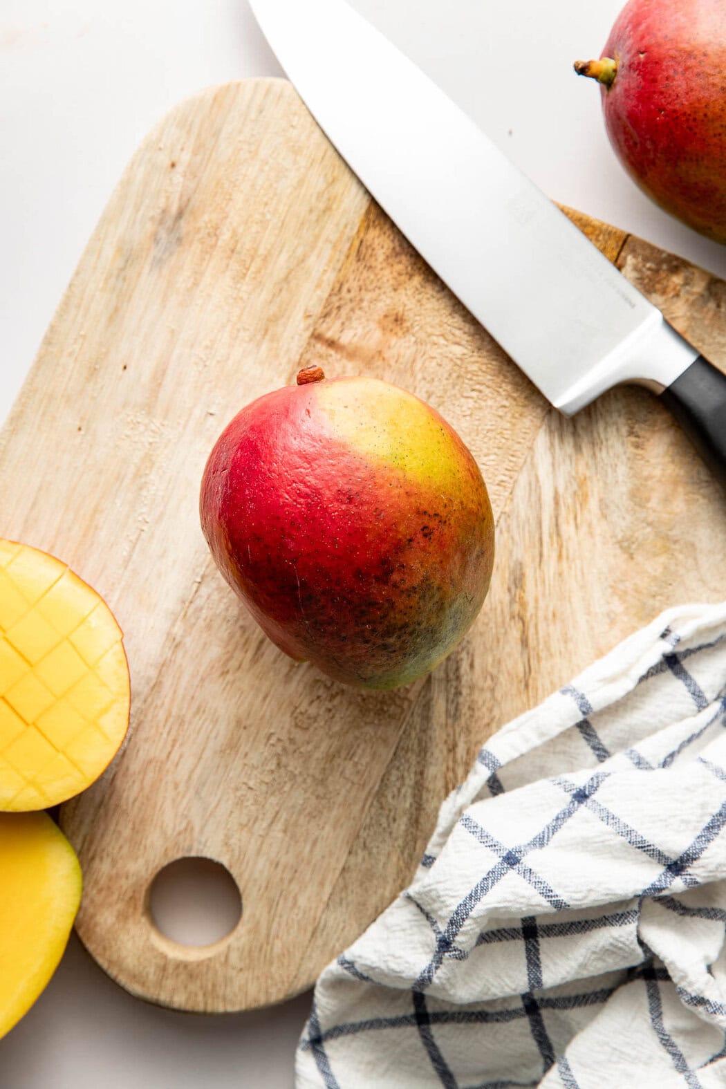 Overhead view of a mango on a wooden cutting board next to a knife.