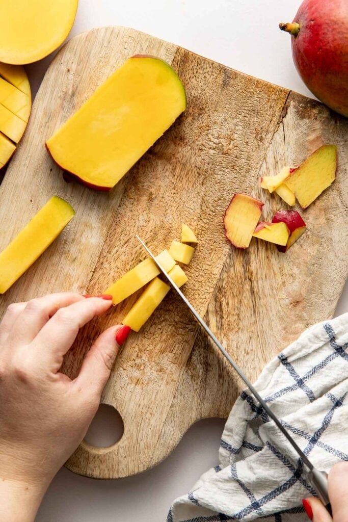 Overhead view of hands cutting a mango on a wooden cutting board.