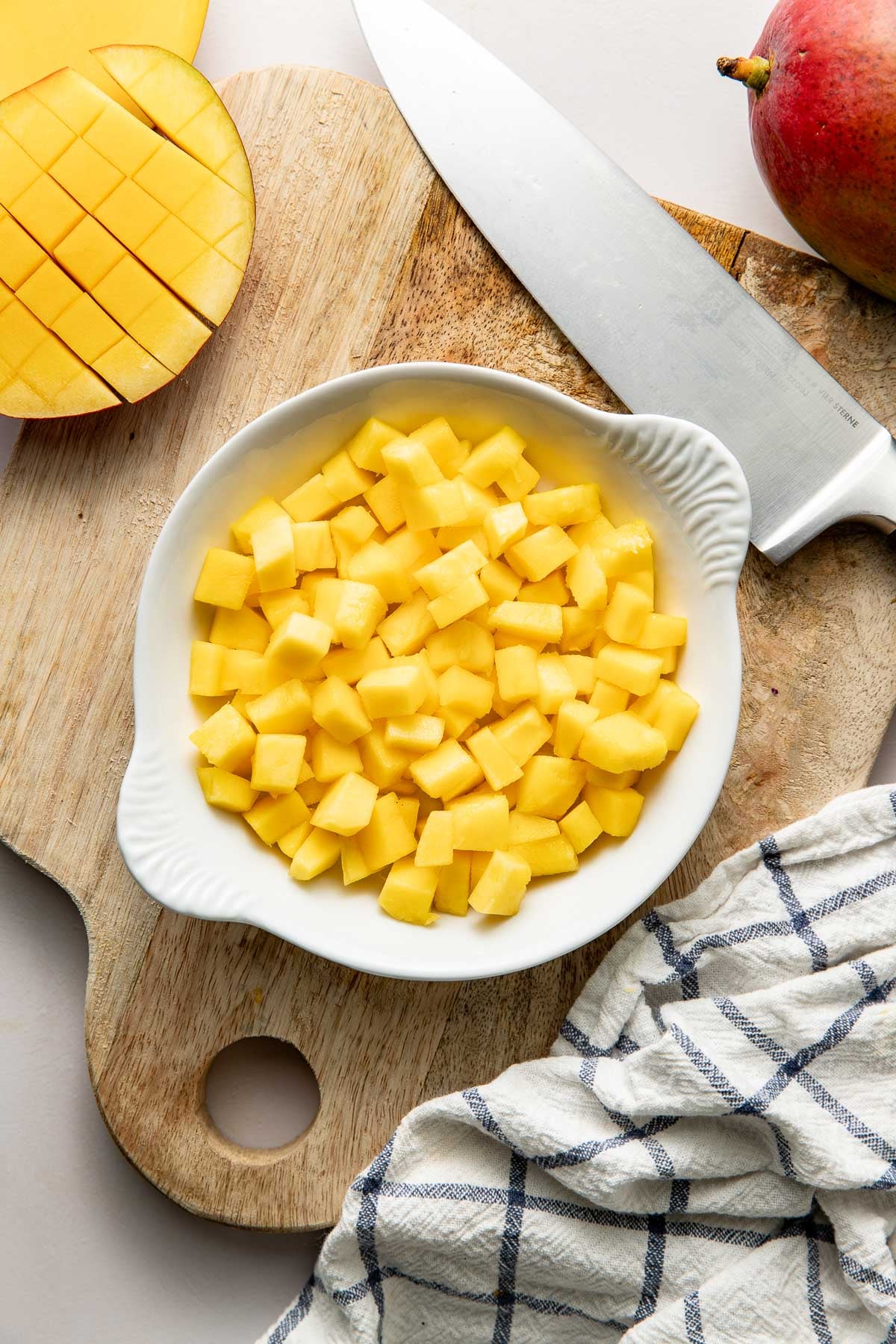 Overhead view of mangos on a wooden cutting board with a knife on the board.