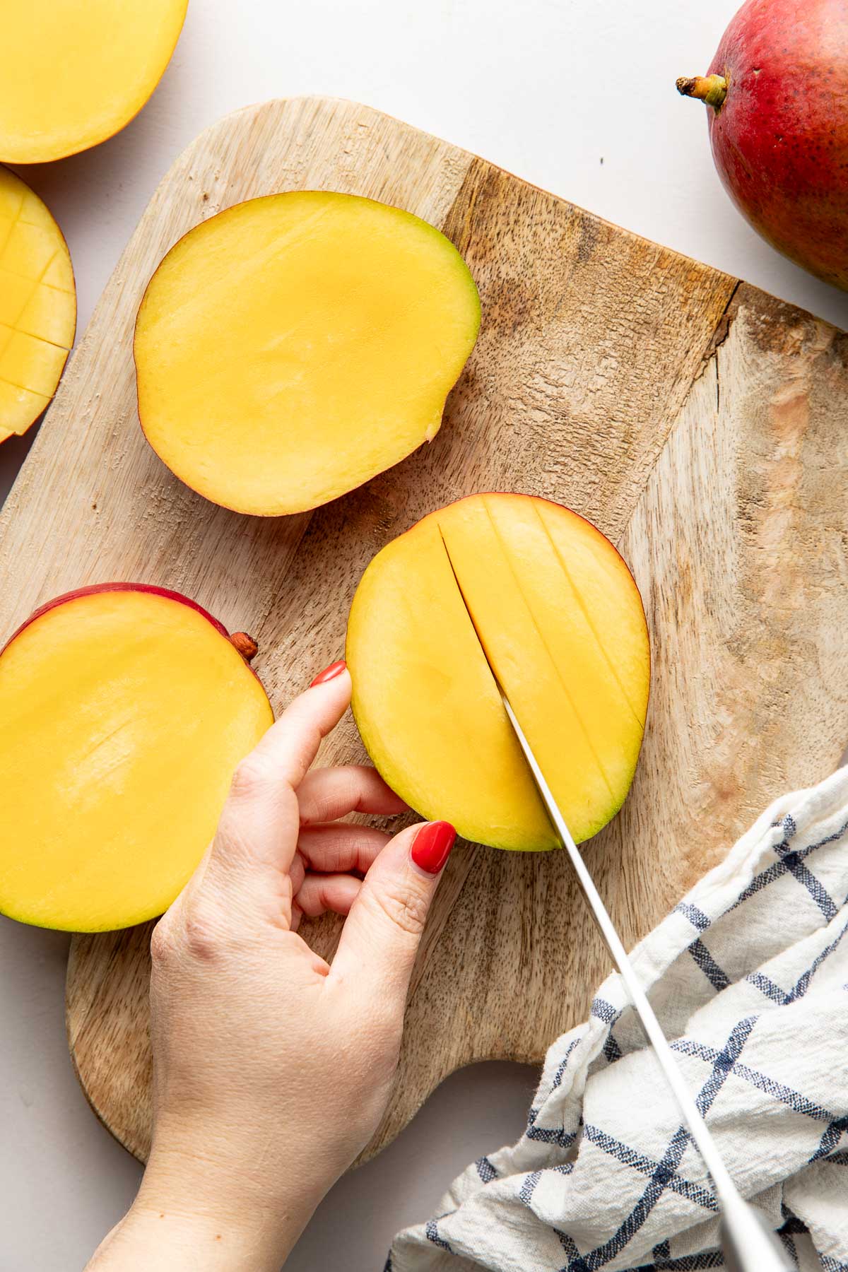 Overhead view of a hand using a knife to slice the inside of a mango.