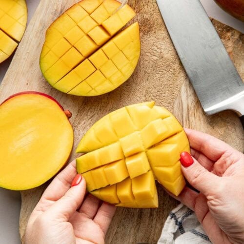 Overhead view of a mango on a cutting board showing various stages of peeling and cutting.