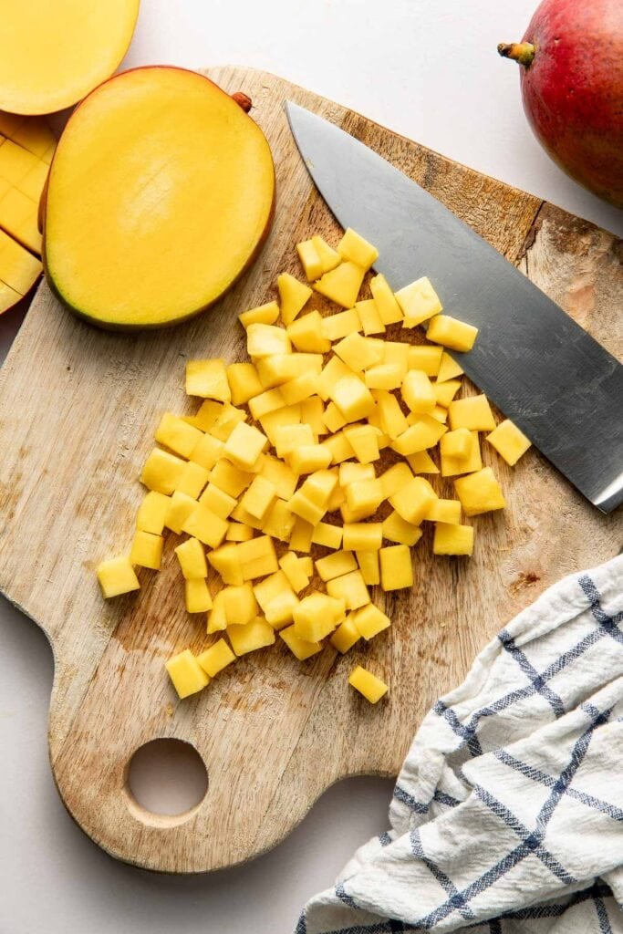 Overhead view of a wooden cutting board filled with small square pieces of mango.