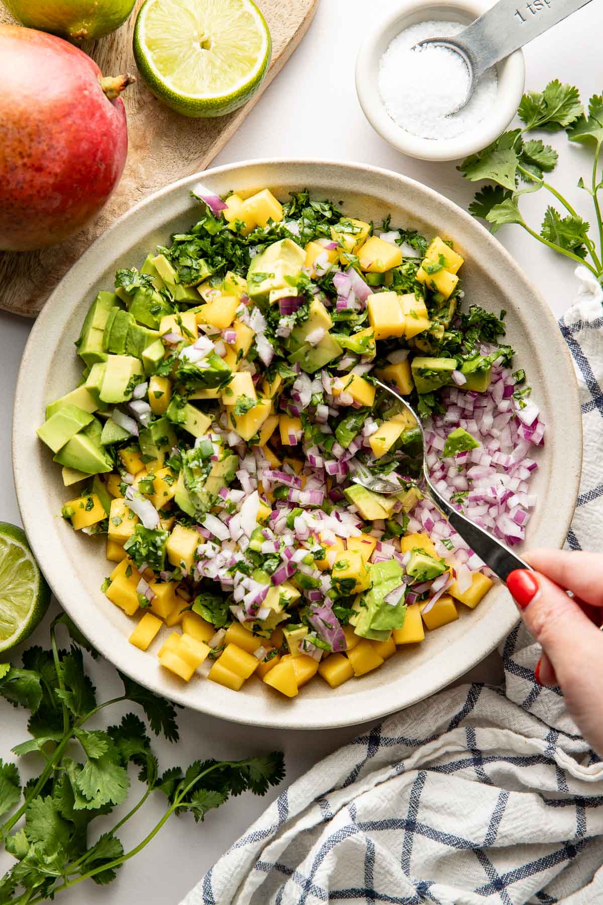 Overhead view of a white bowl of fresh Mango Salsa with a hand stirring the mixture with a spoon.