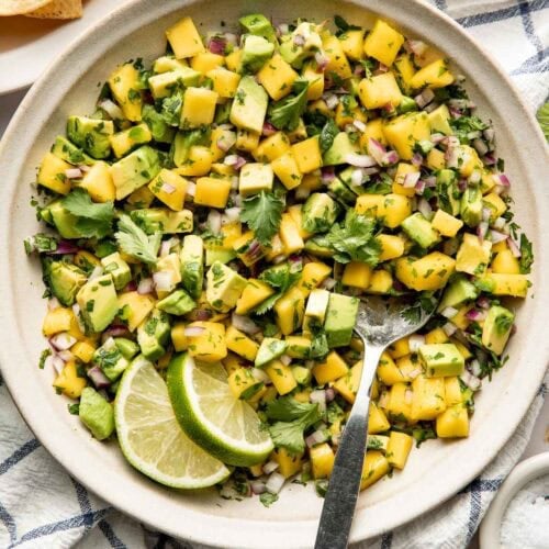 Overhead view of a white bowl of Mango Salsa garnished with limes.
