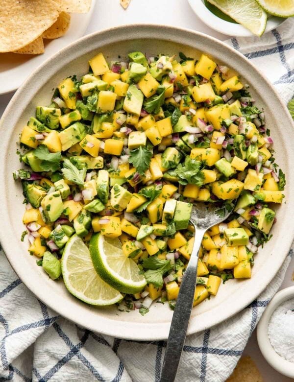 Overhead view of a white bowl of Mango Salsa garnished with limes.